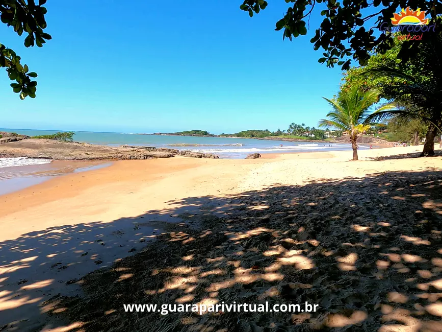 Praia dos Adventistas, em Guarapari: areia dourada &agrave; sombra das &aacute;rvores, mar calmo e pedras na ponta da praia