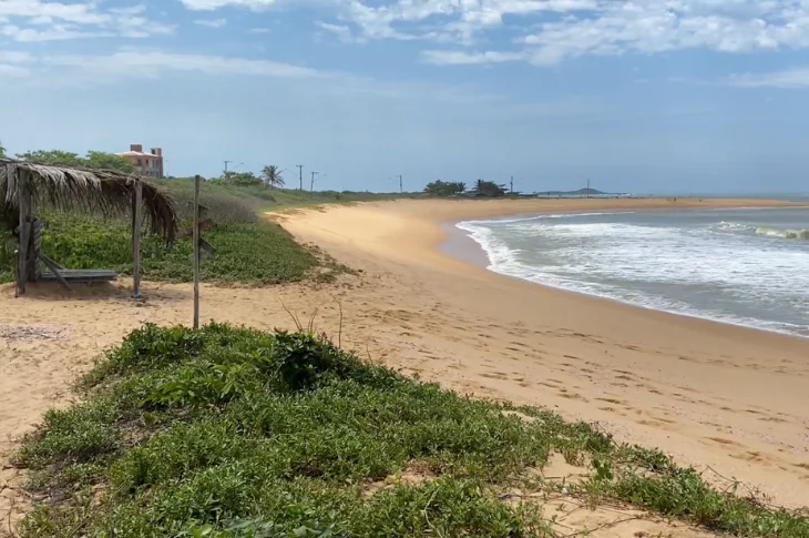Praia de Setiba Pina, em Guarapari, com faixa de areia larga, vegeta&ccedil;&atilde;o de restinga e mar azul