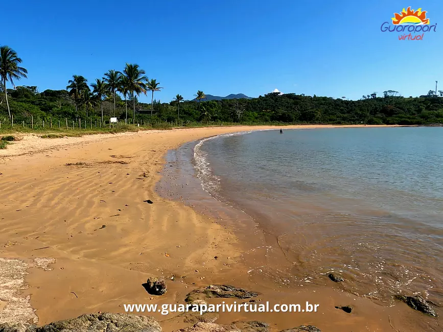 Mar calmo e raso na Praia da Leontina, em Guarapari, com areia dourada, coqueiros e mata ao fundo