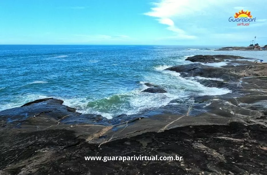 Cost&atilde;o de pedras escuras com ondas batendo, no Centro de Guarapari