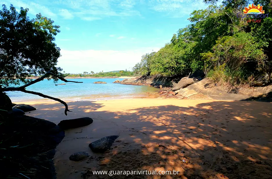 Areia da Praia do Morcego &agrave; sombra das &aacute;rvores, com o mar calmo ao fundo, em Guarapari