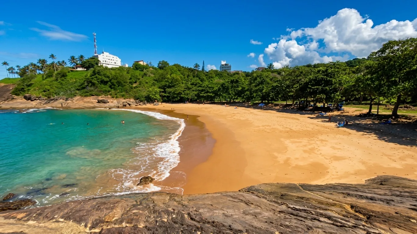 Vista panor&acirc;mica da Praia dos Padres, com mar verde e transparente, areia dourada e &aacute;rvores, em Guarapari