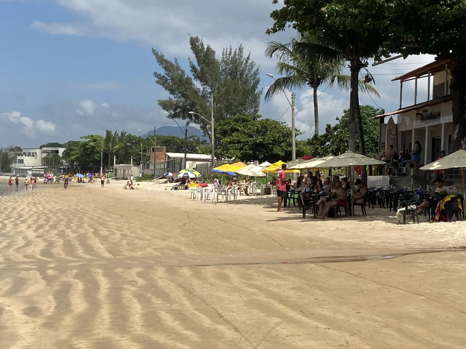 Orla da Praia de Santa M&ocirc;nica com a Cabana Gaivota &agrave; direita, entre &aacute;rvores e mesas na areia, em Guarapari