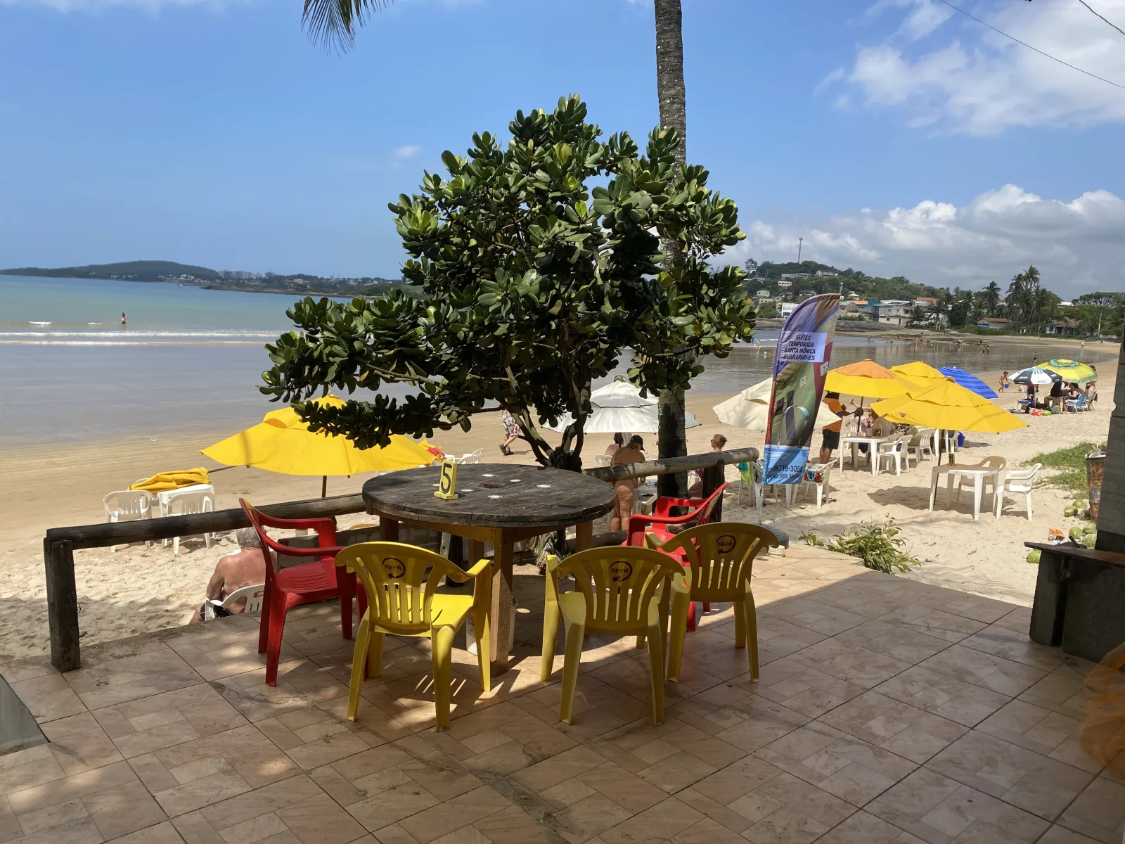 Mesa de madeira e cadeiras coloridas na varanda da Cabana Gaivota, com vista para a Praia de Santa M&ocirc;nica, Guarapari