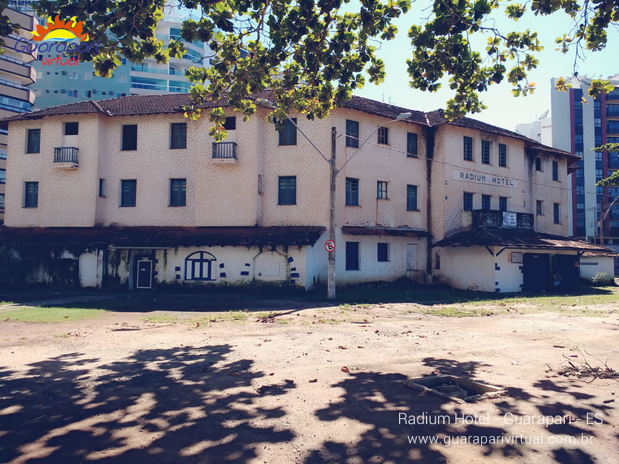 Fachada lateral do Radium Hotel com janelas fechadas, cercado de &aacute;rvores e pr&eacute;dios no Centro de Guarapari