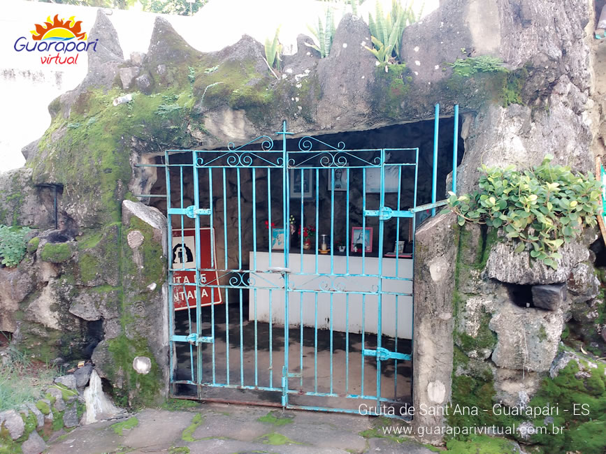 Port&atilde;o azul de ferro na entrada da Gruta de Sant'Ana, em Guarapari, cercada de pedras com musgo e plantas