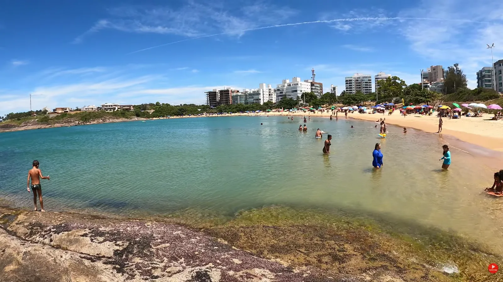 Praia da Bacutia, em Nova Guarapari, com mar calmo e cristalino entre as pedras e pr&eacute;dios na orla