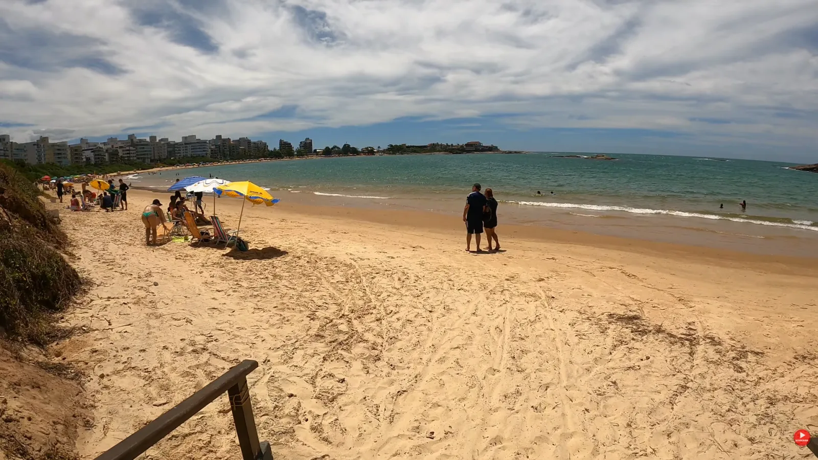 Faixa de areia da Praia de Peracanga, em Nova Guarapari, com guarda-s&oacute;is e pr&eacute;dios ao fundo
