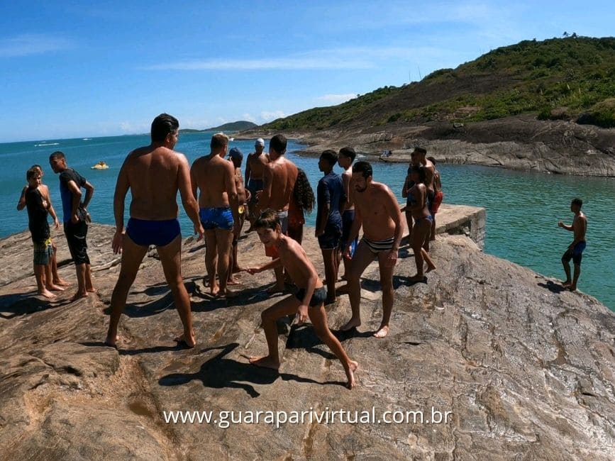 Grupo de jovens esperando a vez de saltar no alto da Pedra do Mero, no ver&atilde;o, em Guarapari