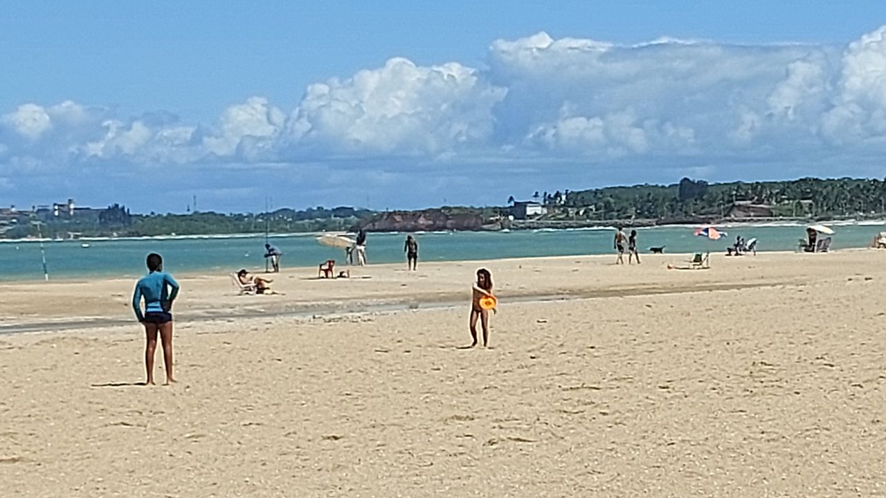 Faixa de areia larga na orla de Mea&iacute;pe, em Guarapari, com banhistas e pescadores na beira do mar