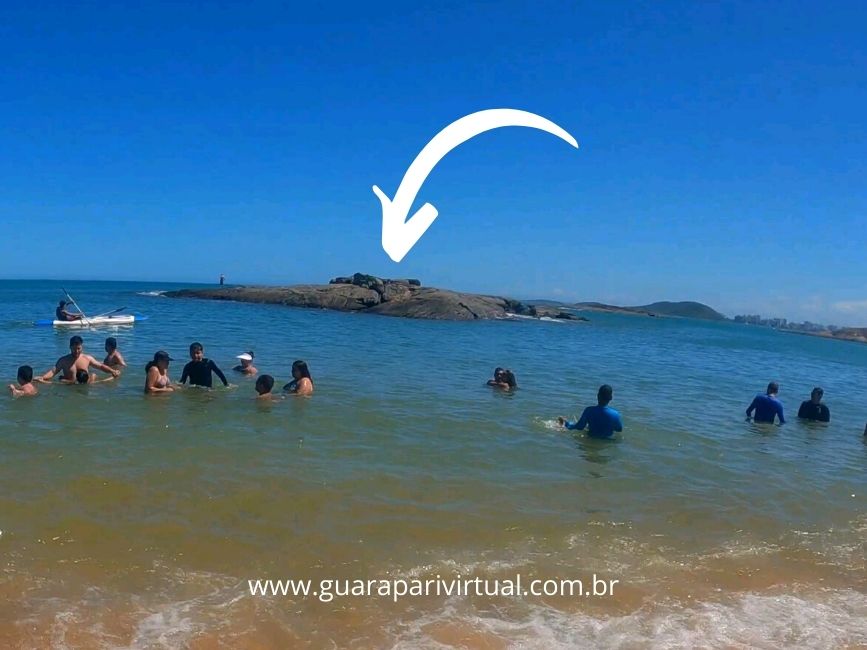 Banhistas no mar calmo da Praia de Setiba, com a Ilha de Setiba, uma forma&ccedil;&atilde;o de pedras, ao fundo